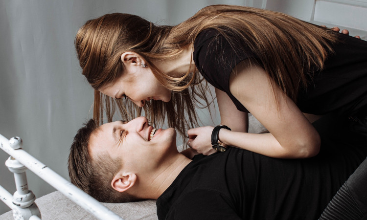 Mulher jovem em cima de homem jovem, ambos sorrindo e se preparando para transar com perguntas picantes.